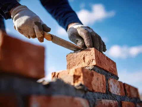 Mason laying a brick on fresh mortar with a trowel